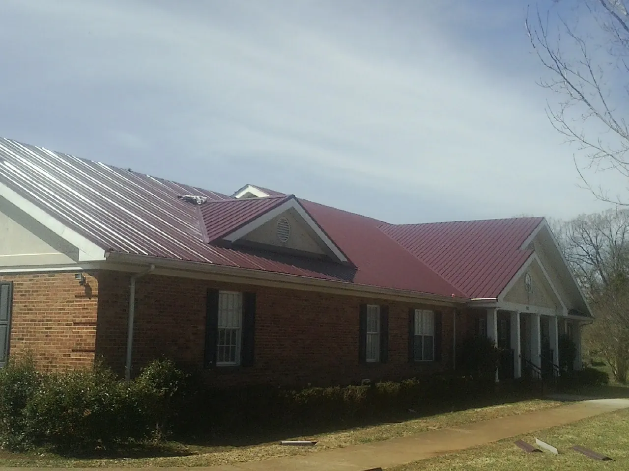 Red metal roof with gabled entries on a long brick building, from a Hail Damage Roof Repair job in Warm Springs
