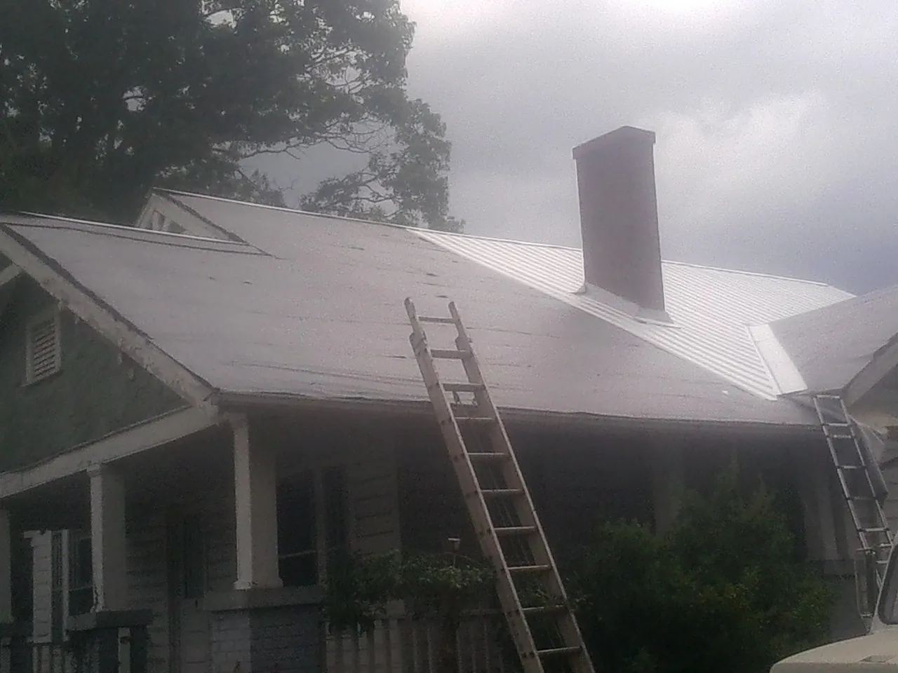 Ladders against a metal roof on an older home with a brick chimney in Warm Springs