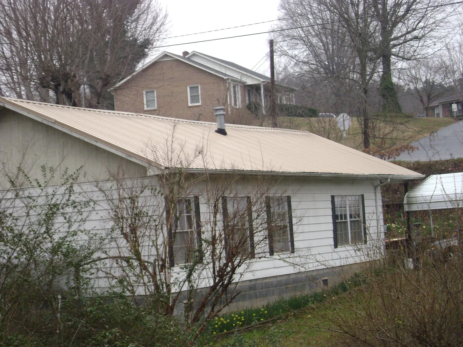 Tan metal roof on a white sided house set into a hillside — Commercial Roofing by Roofing Brothers in Warm Springs